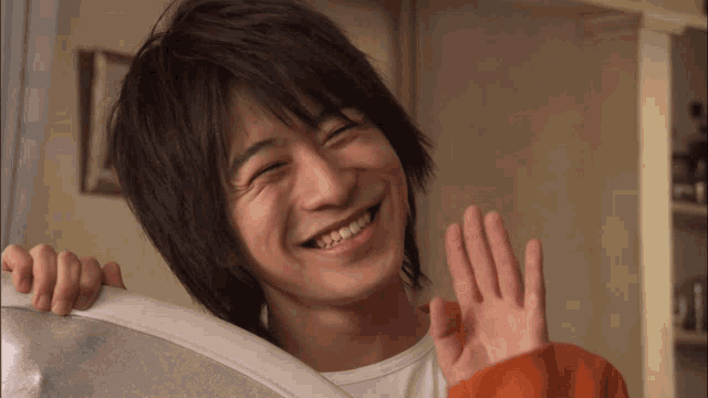 a man with long hair is smiling and waving at the camera