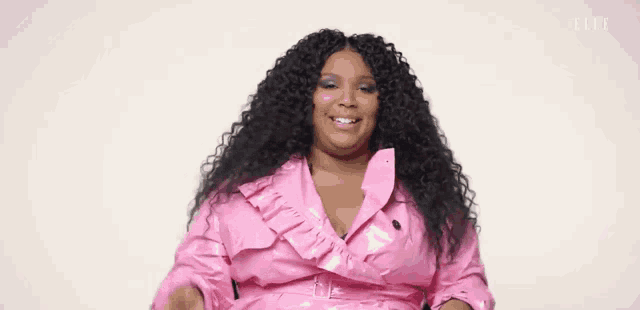 a woman with curly hair is wearing a pink jacket and sitting in a chair .