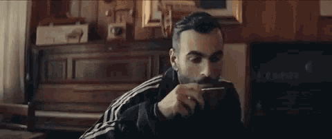a man with a beard is drinking from a cup while sitting in a chair .