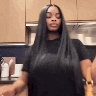 a woman with long black hair is standing in a kitchen holding a knife .
