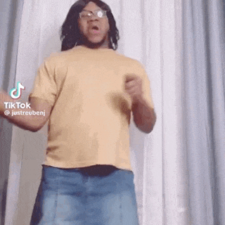 a man in a yellow shirt and a blue skirt is dancing in front of a white curtain .
