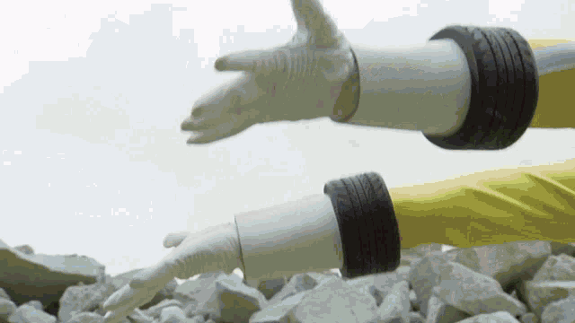 a person wearing white gloves and a yellow jacket is standing on rocks .