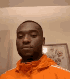 a man in an orange jacket is standing in front of a picture .