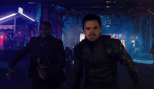 a man in a suit and a man in a black suit are walking down a dark street