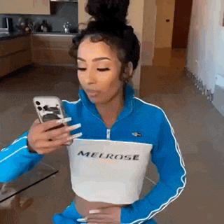 a woman in a blue and white crop top is looking at her phone .