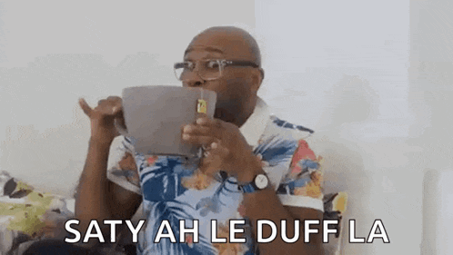 a man wearing glasses is sitting on a couch holding a tablet in his hand and making a funny face .