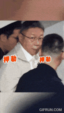 a man in a suit and tie is surrounded by other men with chinese writing on the bottom right
