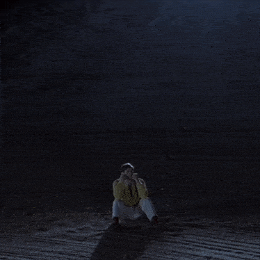 a man in a yellow jacket and tie is kneeling in the rain