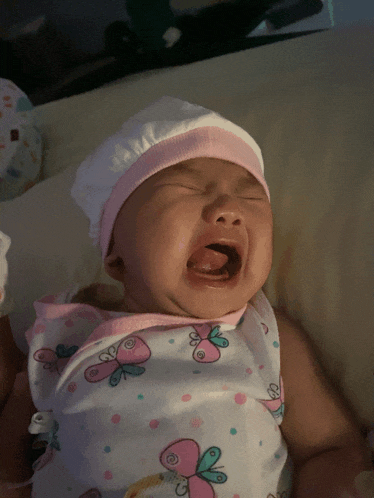 a baby wearing a white hat and a pink butterfly outfit is crying