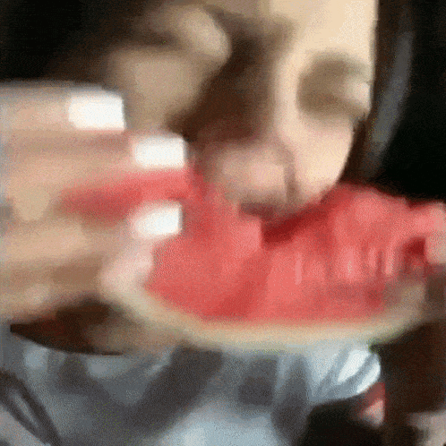 a person is eating a slice of watermelon with their eyes closed