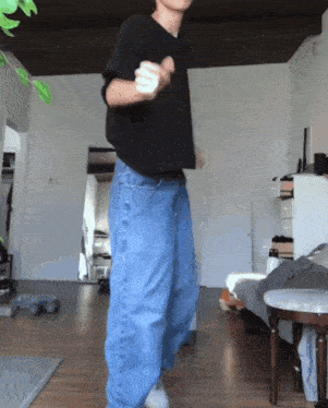 a man in a black shirt and blue jeans is dancing in a room