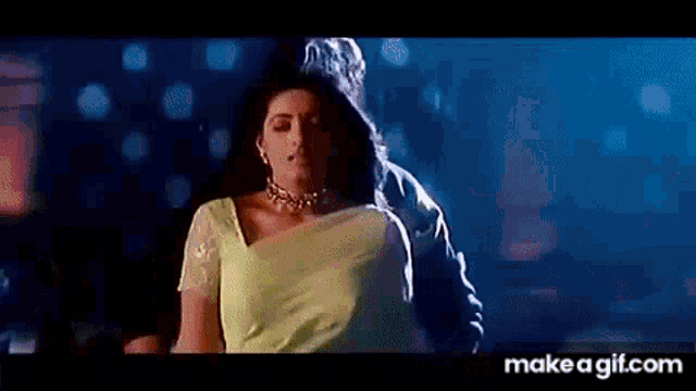 a man is holding a woman in a yellow saree in a dark room .
