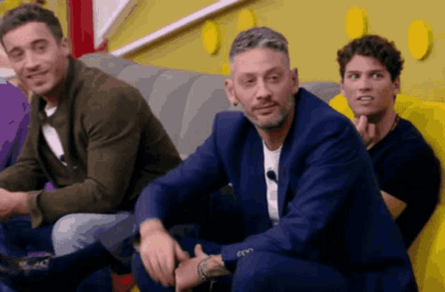 three men are sitting on a couch and one is wearing a suit