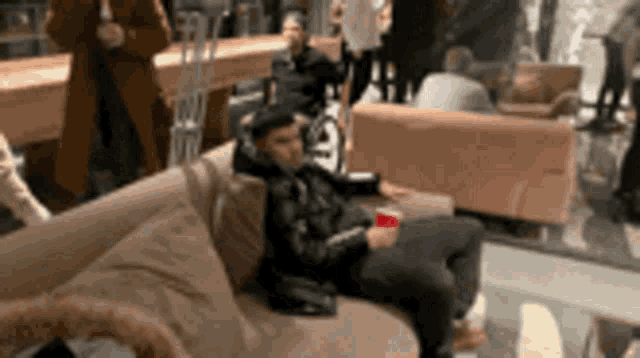 a man is sitting on a couch holding a red cup in a crowded room .