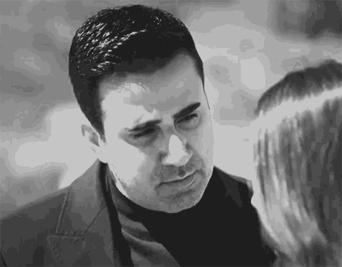 a man in a suit and turtleneck is looking at a woman .