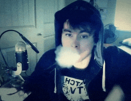 a man wearing a shirt that says hot vt is blowing smoke