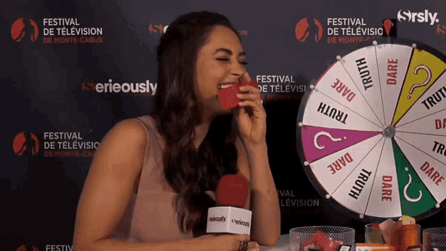 a woman laughs in front of a spinning wheel that says dare