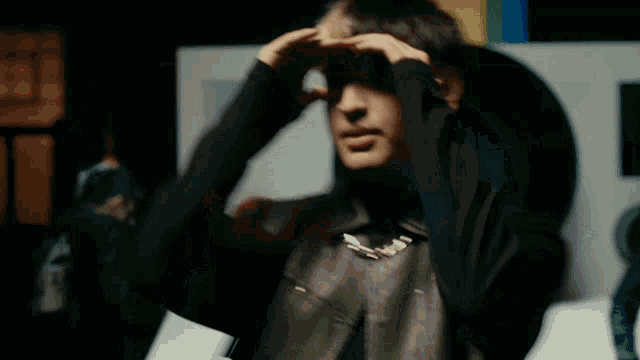a man in a leather jacket is covering his face with his hand