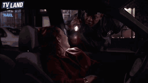 a woman is sleeping in the back seat of a car while a police officer holds a flashlight in front of her
