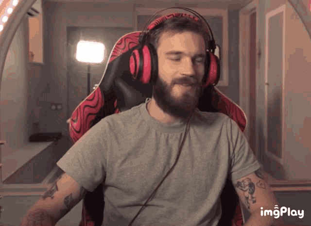 a man with a beard wearing headphones and a gray shirt with a tattoo on his arm says imgplay