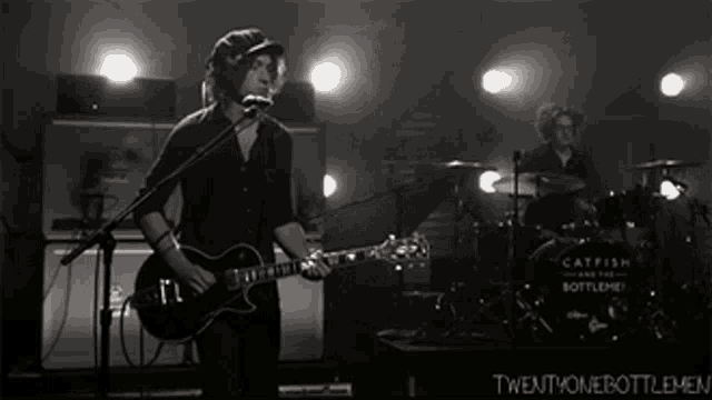 a black and white photo of a man playing a guitar and singing into a microphone