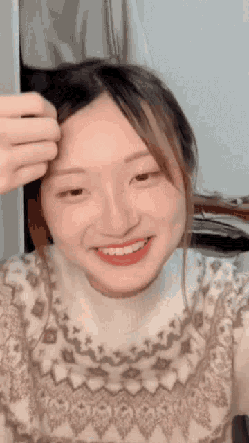 a woman wearing a sweater is smiling and touching her hair
