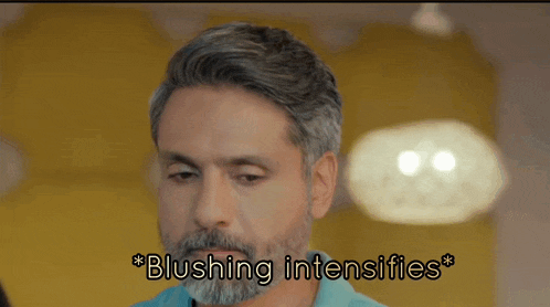 a man with a beard says blushing intensifies in front of a yellow wall