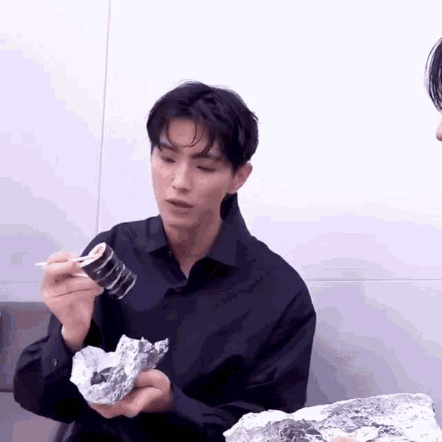 a man in a black shirt is eating a roll of sushi