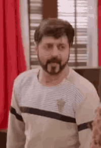 a man with a beard and mustache is standing in front of a window in a room .
