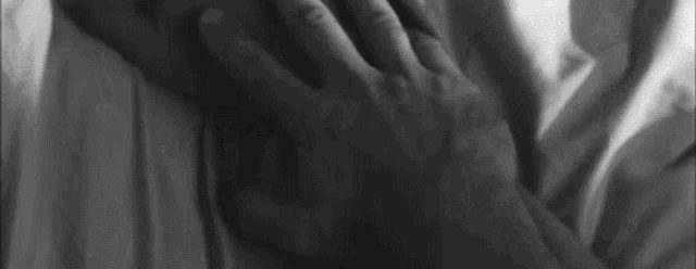 a black and white photo of a person laying on a bed with their hands on their chest .