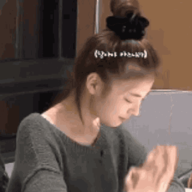 a woman with a bun on her head is sitting at a table with her hands folded .
