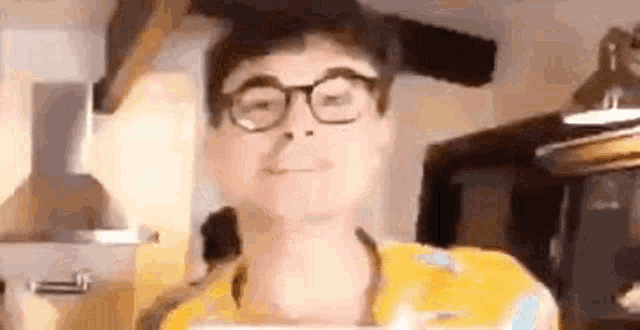 a man wearing glasses and a yellow shirt is standing in a kitchen holding a box .