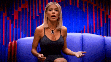 a woman in a black dress is sitting on a blue couch with her hands outstretched .