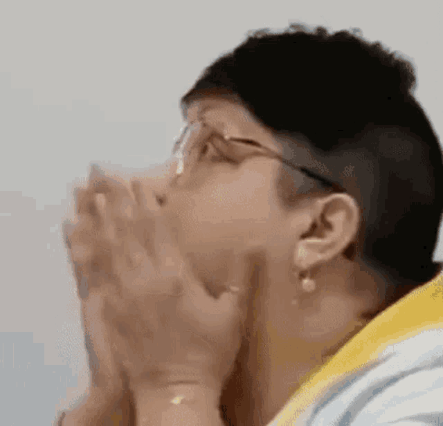 a woman wearing glasses is covering her mouth with her hands while praying .