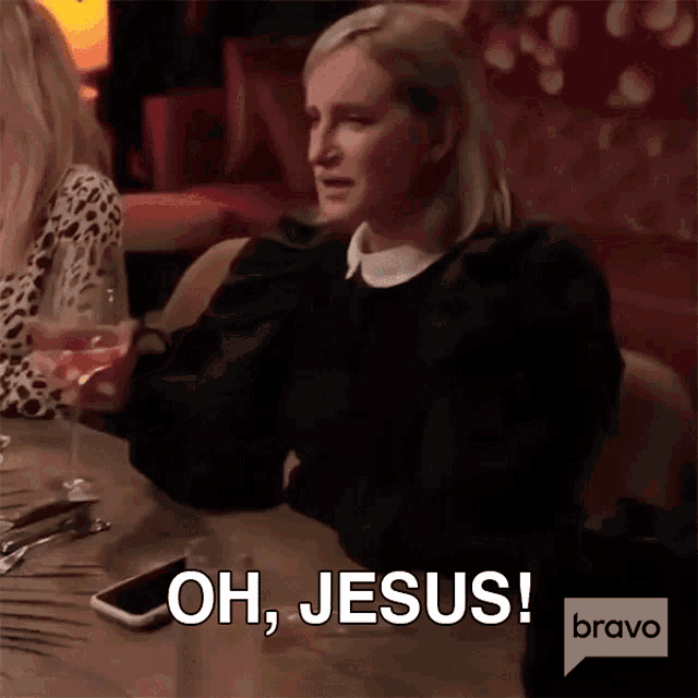 a woman is sitting at a table with a glass of wine and says oh jesus bravo