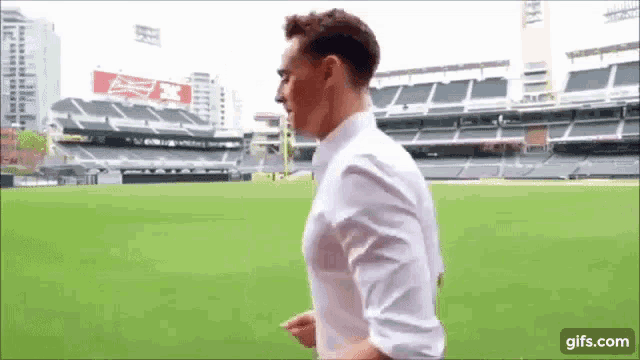 a man in a white shirt is walking across a baseball field .