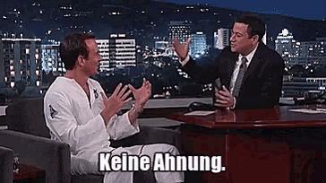 a man sitting in a chair talking to a man in a suit with the words keine ahnung on the bottom