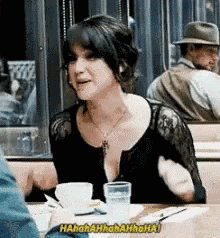 a woman is sitting at a table with a cup of coffee and a glass of water and is laughing .