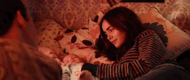 a woman is laying on a couch holding a baby while a man looks on .