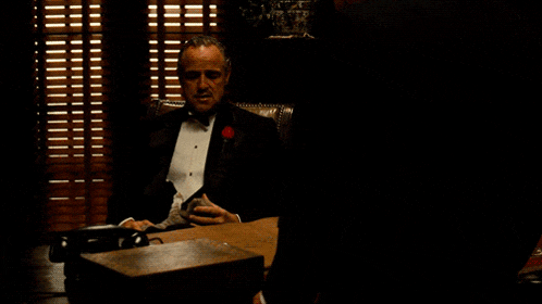 a man in a tuxedo sits at a desk with a telephone