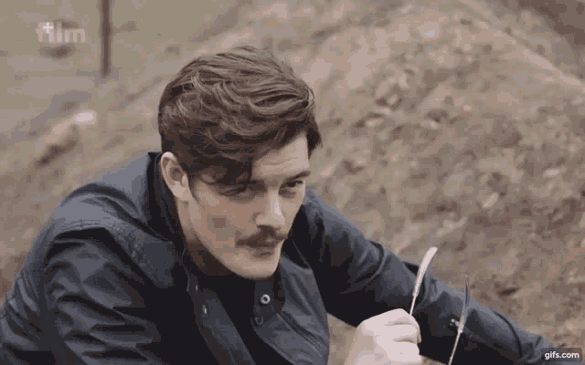 a man with a mustache is holding a knife and the word film is on the screen