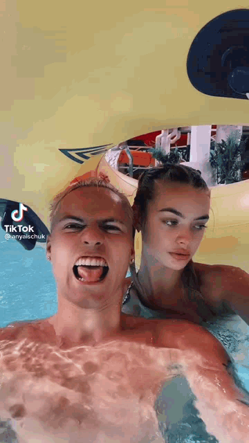 a man and a woman are in a swimming pool and the man is sticking his tongue out .