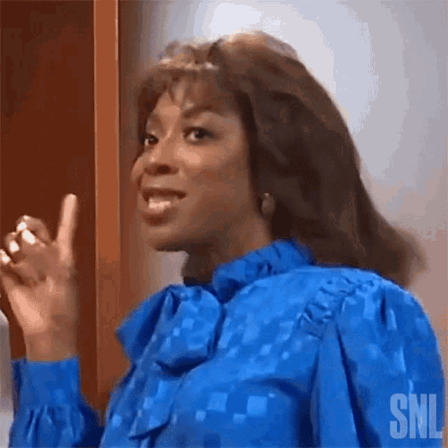 a woman in a blue shirt is pointing her finger up .