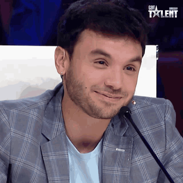 a man sitting in front of a microphone with a got talent logo behind him