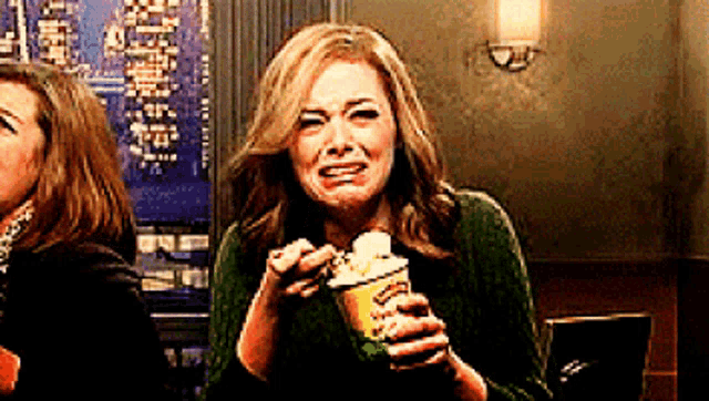 a woman in a green sweater is holding a cup of popcorn and crying