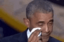 barack obama is crying while holding a tissue in his hand .