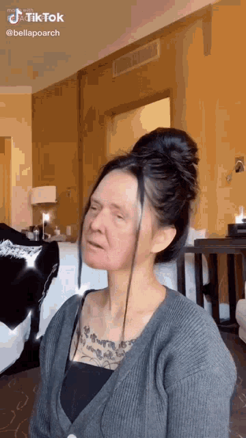 a woman is sitting in a hotel room with her hair in a bun and a tattoo on her chest .