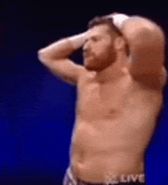 a shirtless wrestler is standing with his hands on his head .