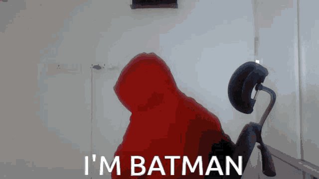 a man in a red hoodie says " i 'm batman " while sitting in an office chair