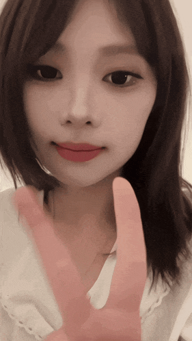 a woman with dark hair and red lips is making a peace sign with her fingers